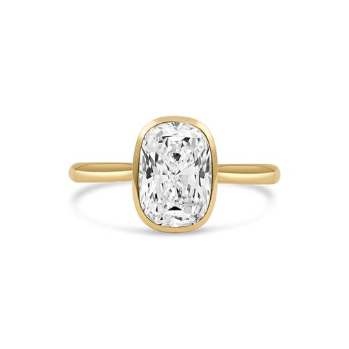 A yellow gold ring featuring n elongated cushion-cut diamond in a bezel setting, shown against a clean white background.