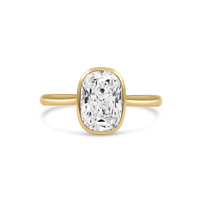 A yellow gold ring featuring n elongated cushion-cut diamond in a bezel setting, shown against a clean white background.